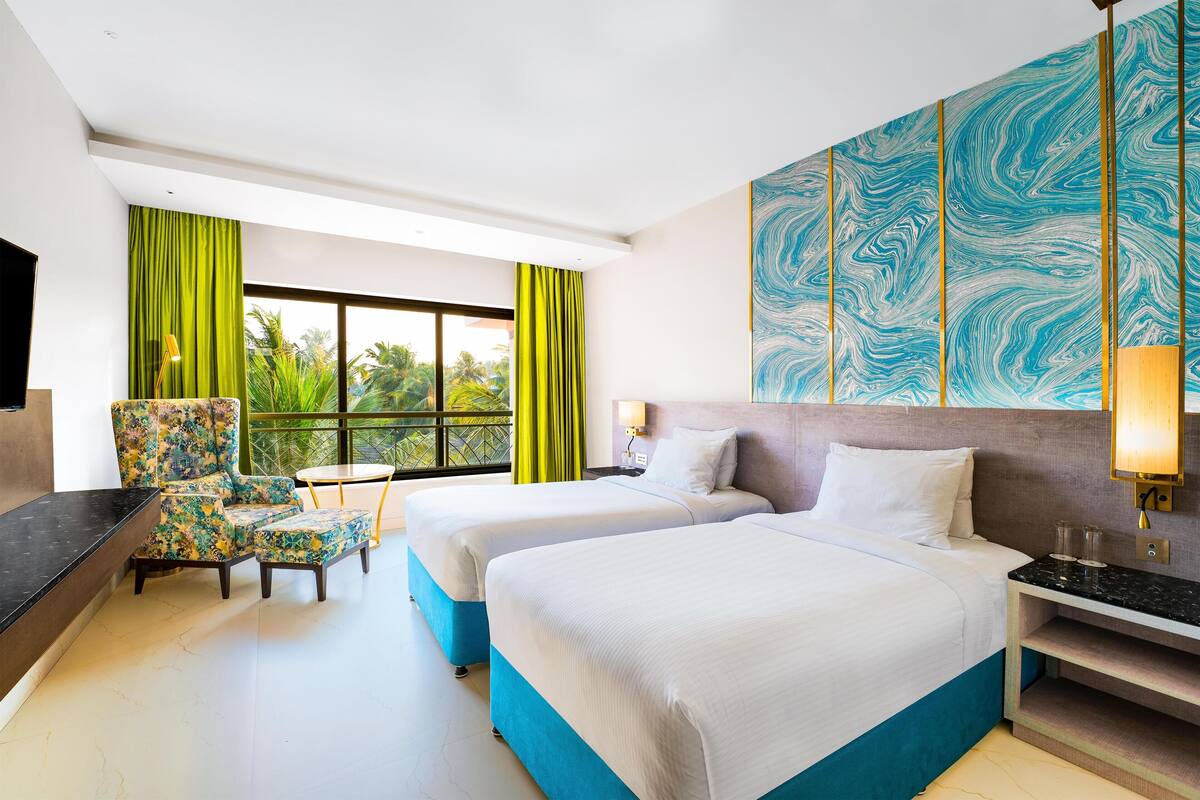 A hotel room with two beds, a desk, a chair, a TV, and a large window with curtains.