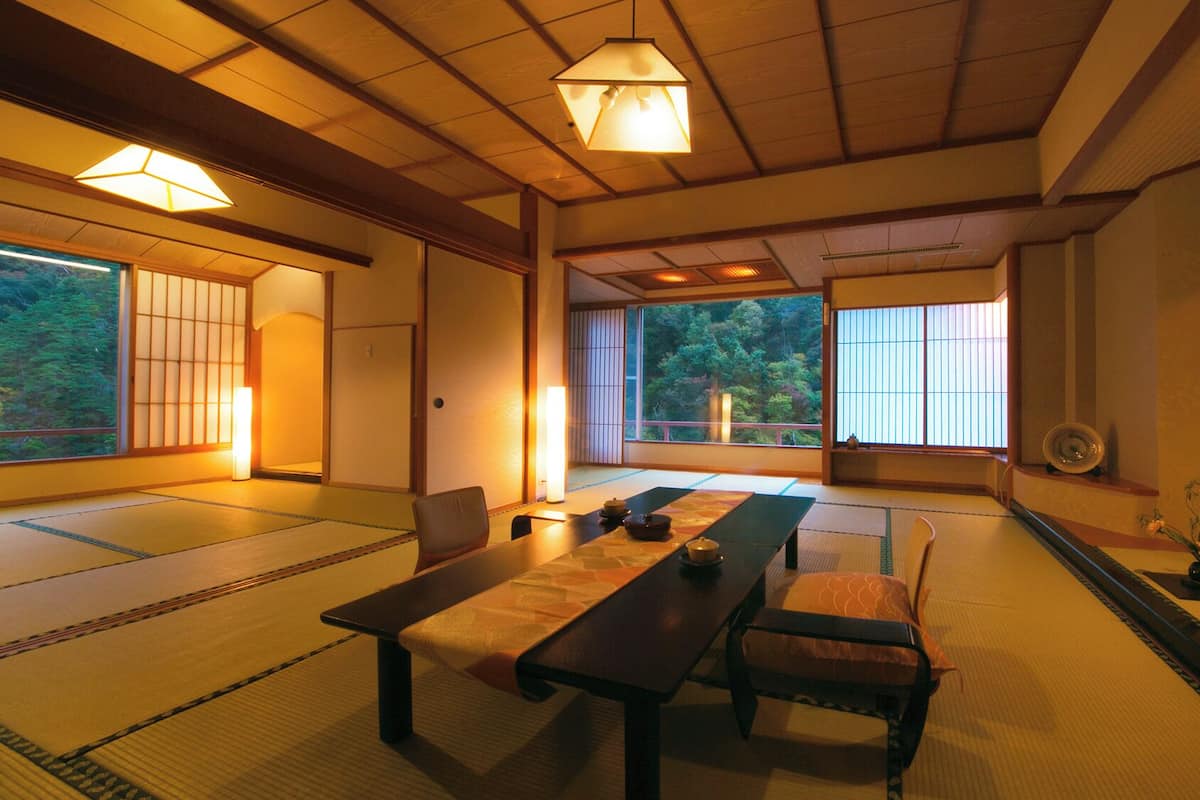 Une pièce de style japonais traditionnel, avec un sol recouvert de tatamis, une table basse, des chaises et des portes coulissantes.