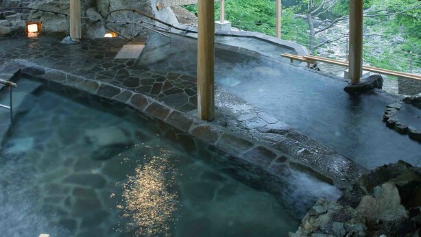 Un área de aguas termales con suelo de piedra, vigas de madera y vistas de vegetación exuberante.