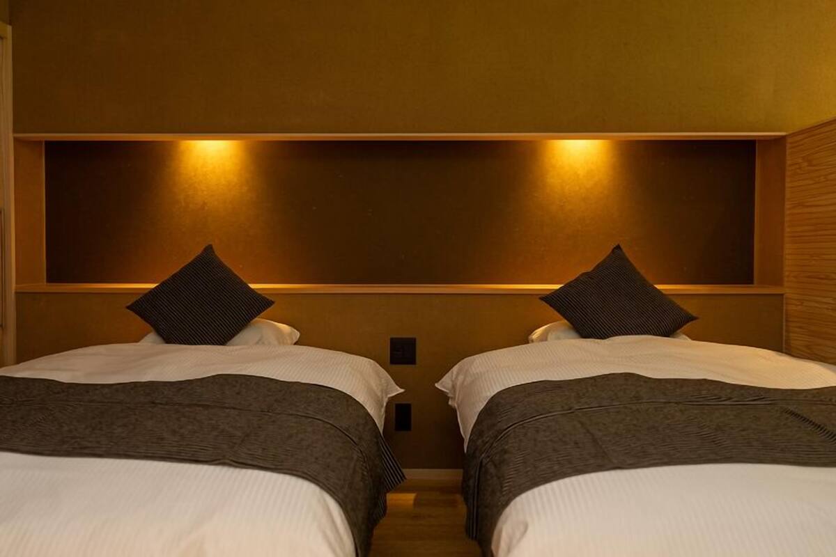 Une chambre d’hôtel avec deux lits, une tête de lit en bois et un luminaire fixé au mur.