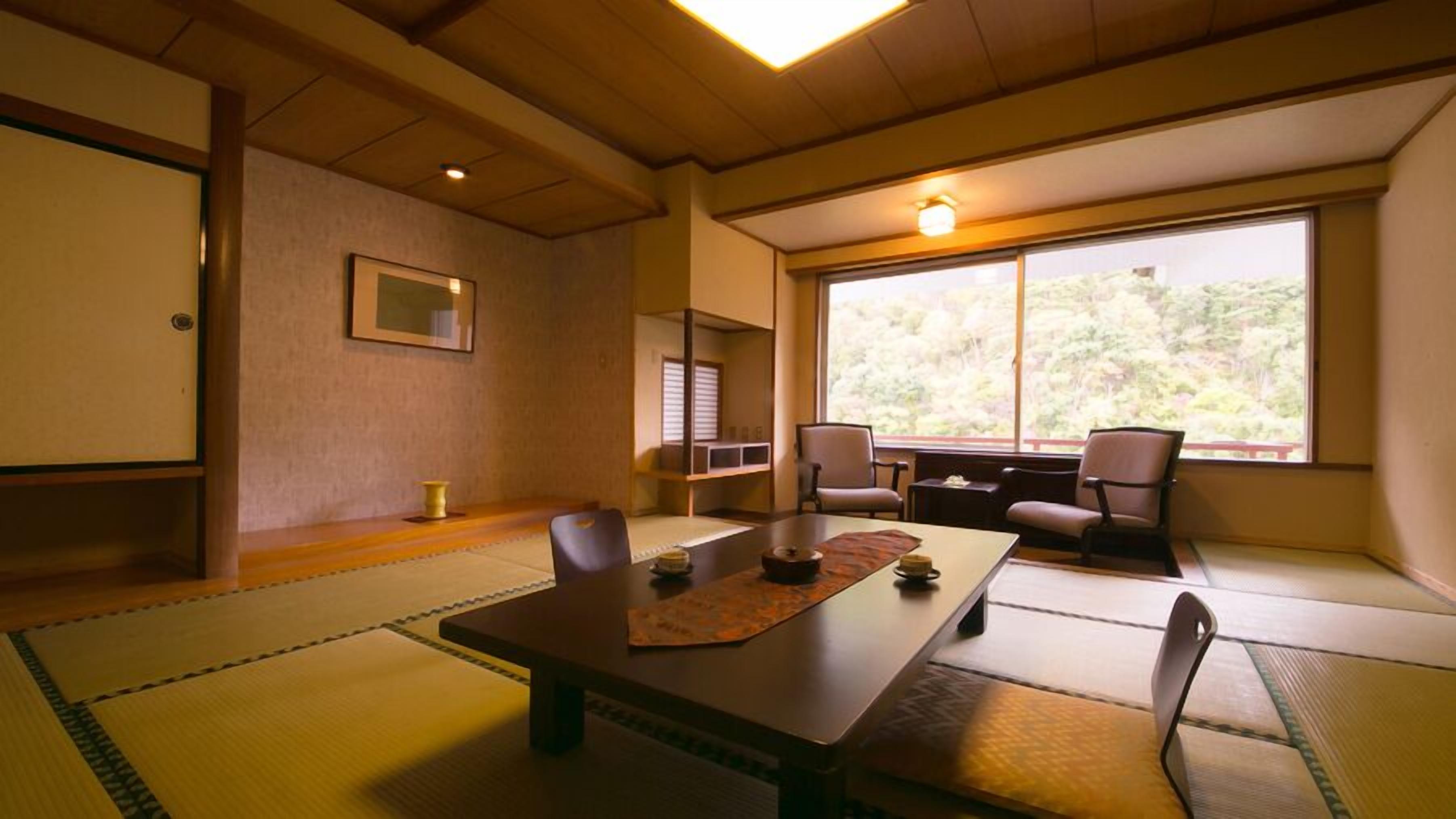 Une pièce de style japonais traditionnel, avec un sol recouvert de tatamis, une table basse, des chaises, une fenêtre donnant sur un paysage verdoyant et un tableau encadré accroché au mur.