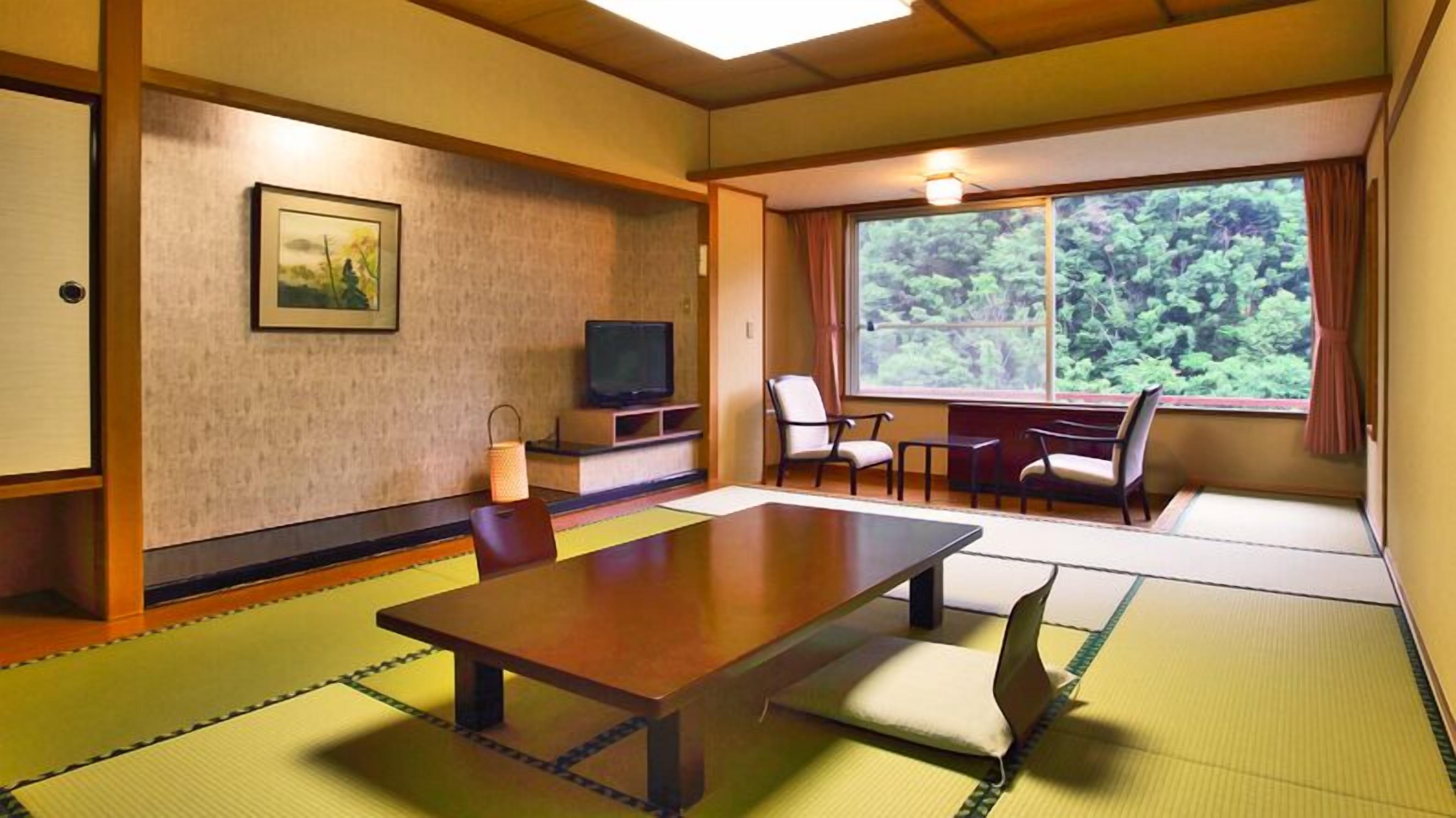 Une pièce de style japonais traditionnel, avec un sol recouvert de tatamis, une table basse, des sièges, un téléviseur et une fenêtre donnant sur un paysage verdoyant.