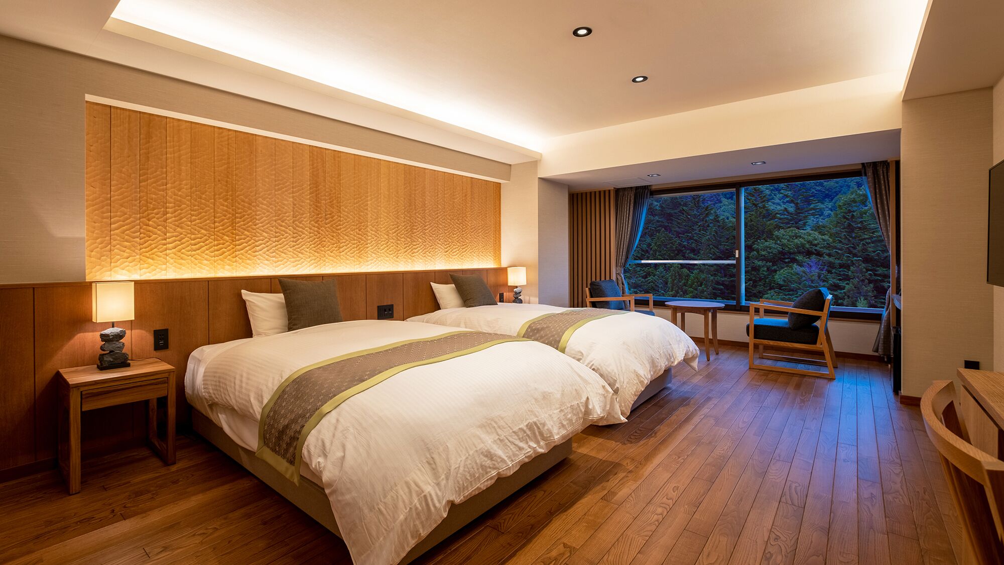 Une chambre d’hôtel avec un grand lit, un bureau, une chaise et une fenêtre donnant sur les arbres.