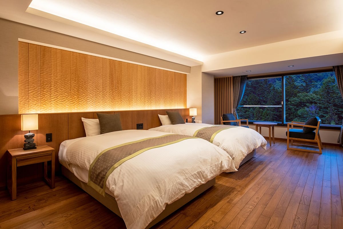 Une chambre d’hôtel avec un grand lit, un bureau, une chaise et une fenêtre donnant sur les arbres.