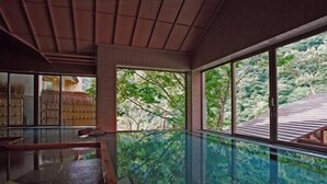 Una habitación con piscina de fondo de cristal, ventanas amplias y vistas al verdor exterior.