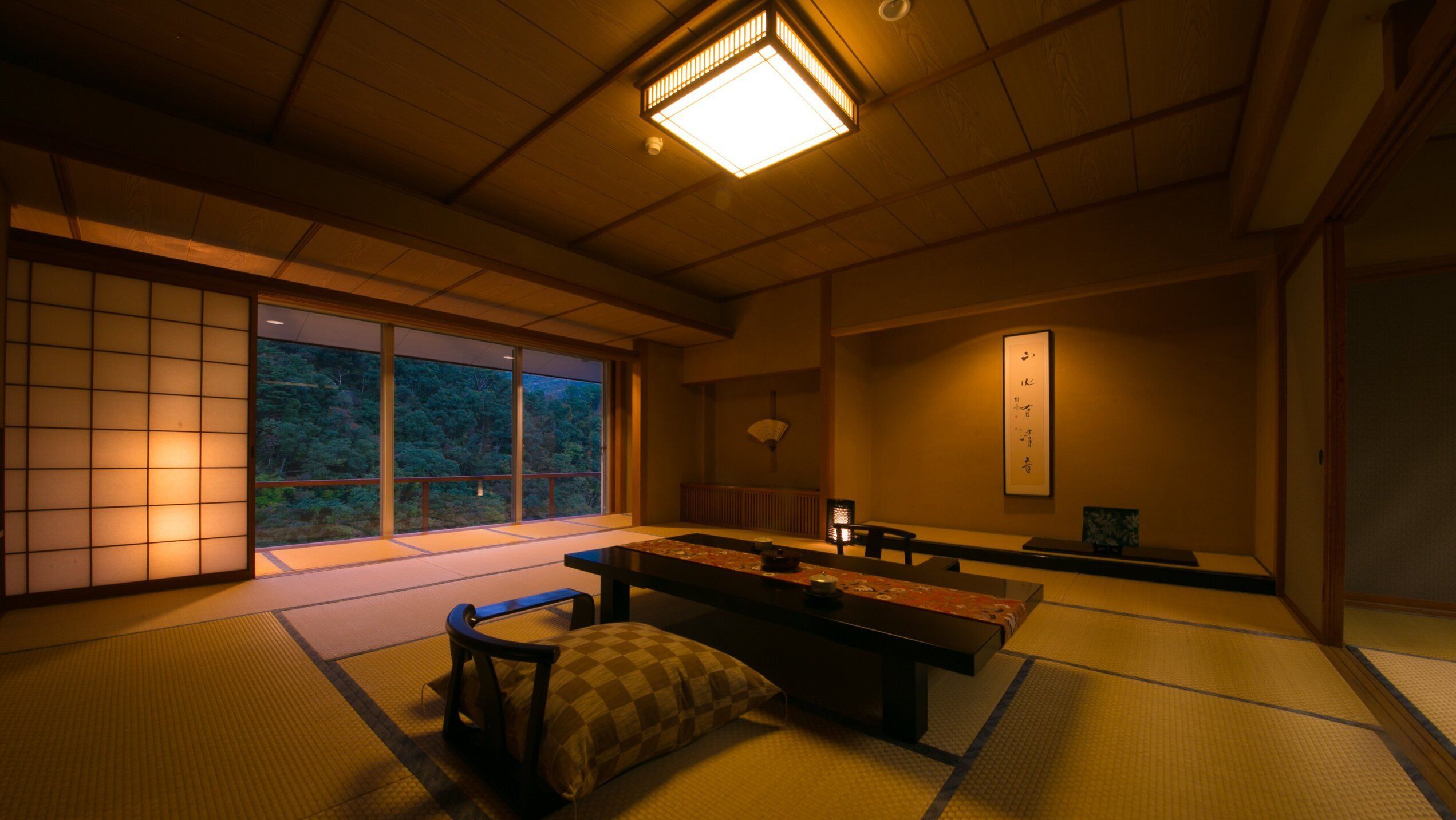 Une pièce de style japonais traditionnel, avec un sol recouvert de tatamis, une table basse et une vue sur une forêt, visible à travers de grandes fenêtres.