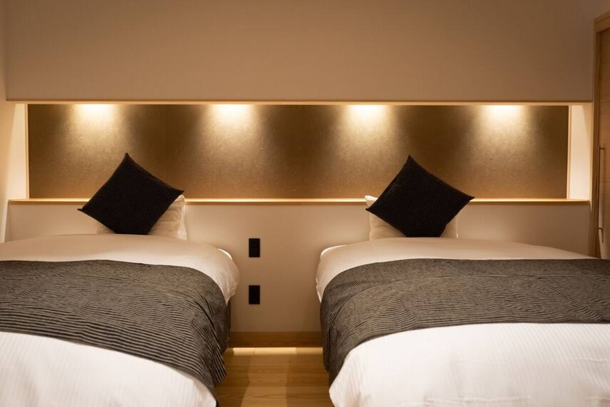 Une chambre d’hôtel avec deux lits, une tête de lit dotée d’un éclairage intégré et un plancher en bois.