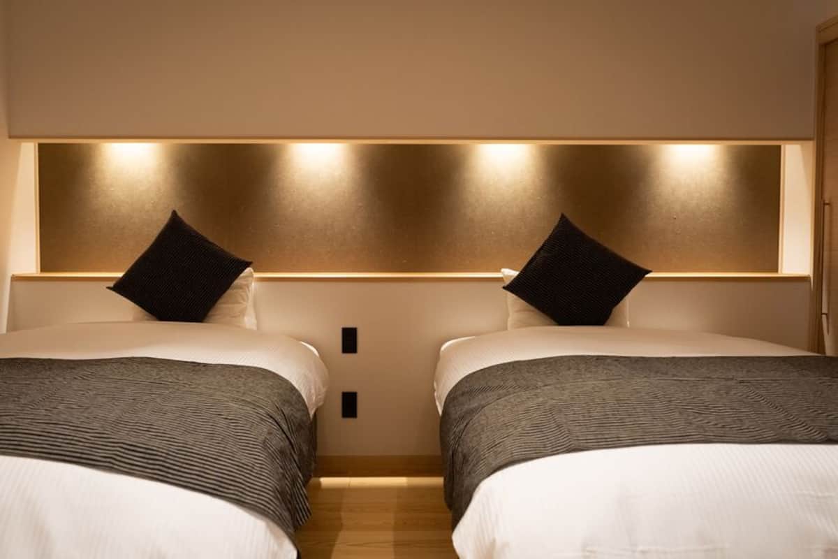 A hotel room with two beds, a headboard with integrated lighting, and a wooden floor.