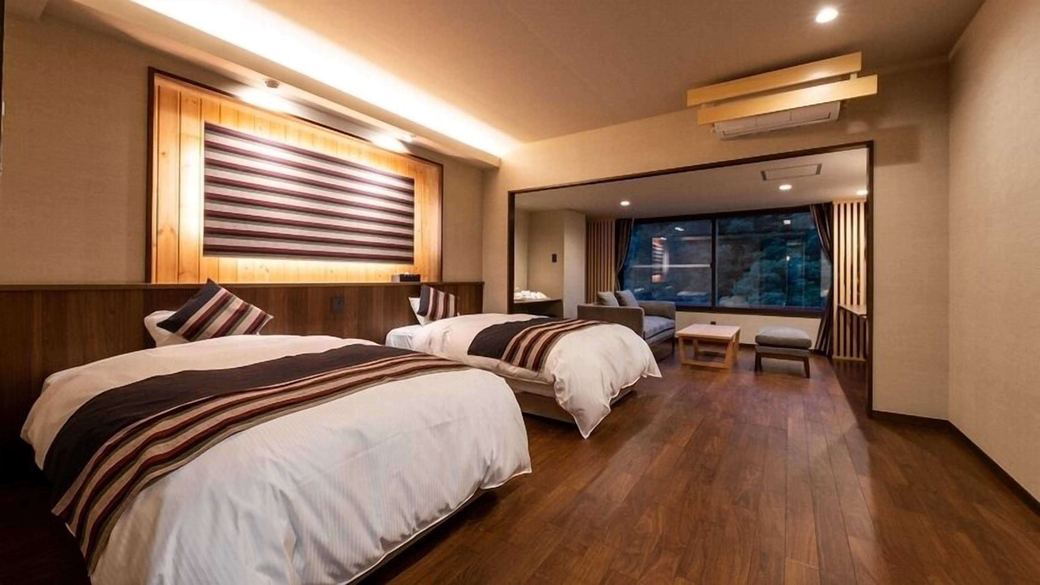 Une chambre d’hôtel avec deux lits, un canapé, une petite table et une vue sur l’extérieur.