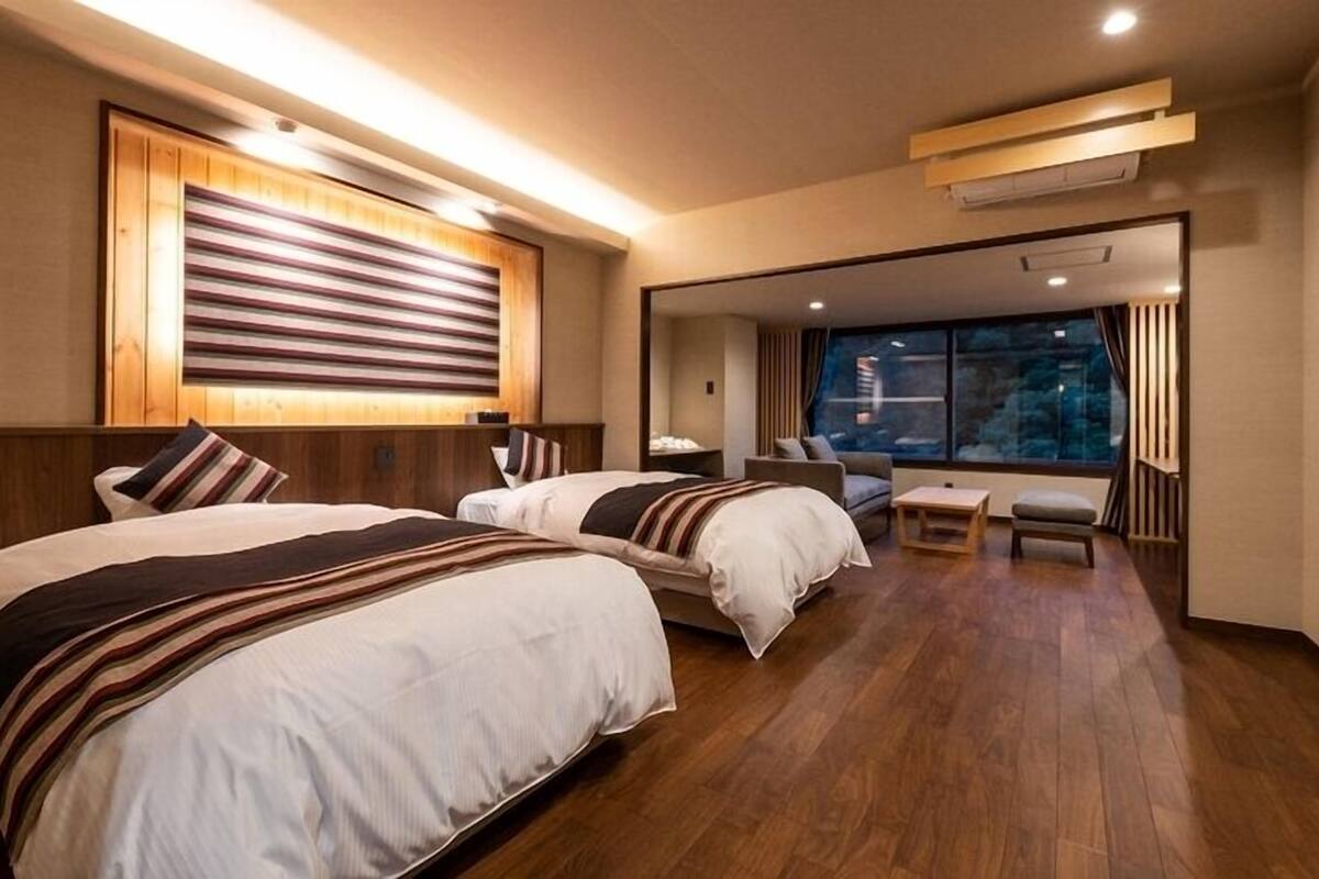 Une chambre d’hôtel avec deux lits, un canapé, une petite table et une vue sur l’extérieur.