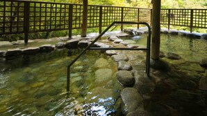 Un onsen japonés tradicional con una terraza de madera, escalones de piedra y una cerca de bambú.