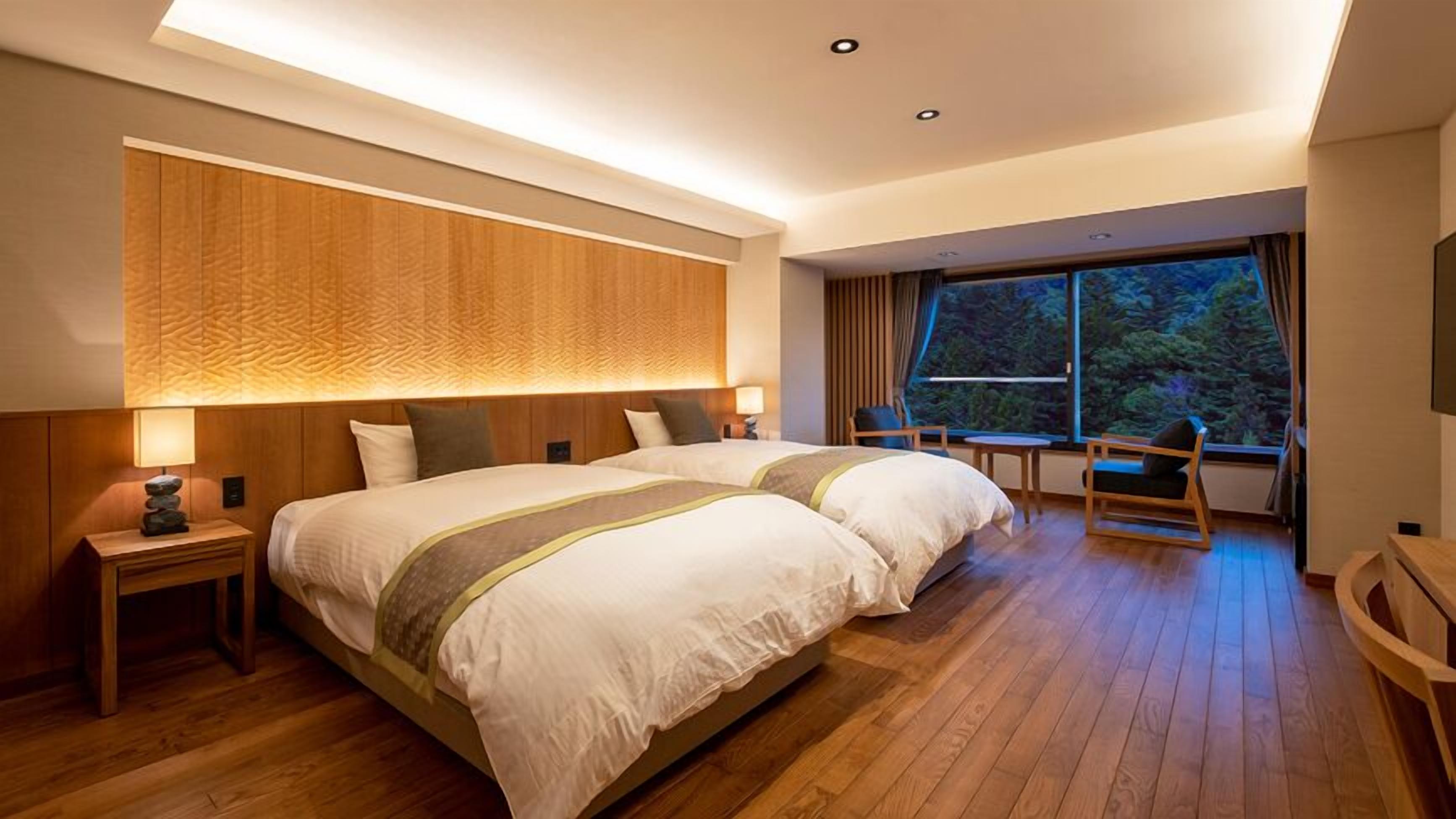 Une chambre d’hôtel moderne, dotée d’un grand lit, de tables de chevet, d’une petite table et offrant une vue sur l’extérieur.