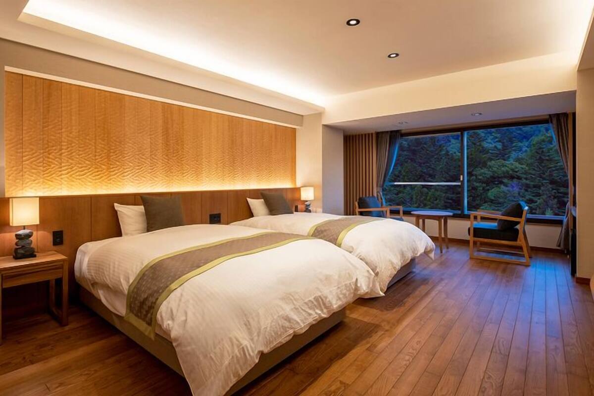 Une chambre d’hôtel moderne, dotée d’un grand lit, de tables de chevet, d’une petite table et offrant une vue sur l’extérieur.
