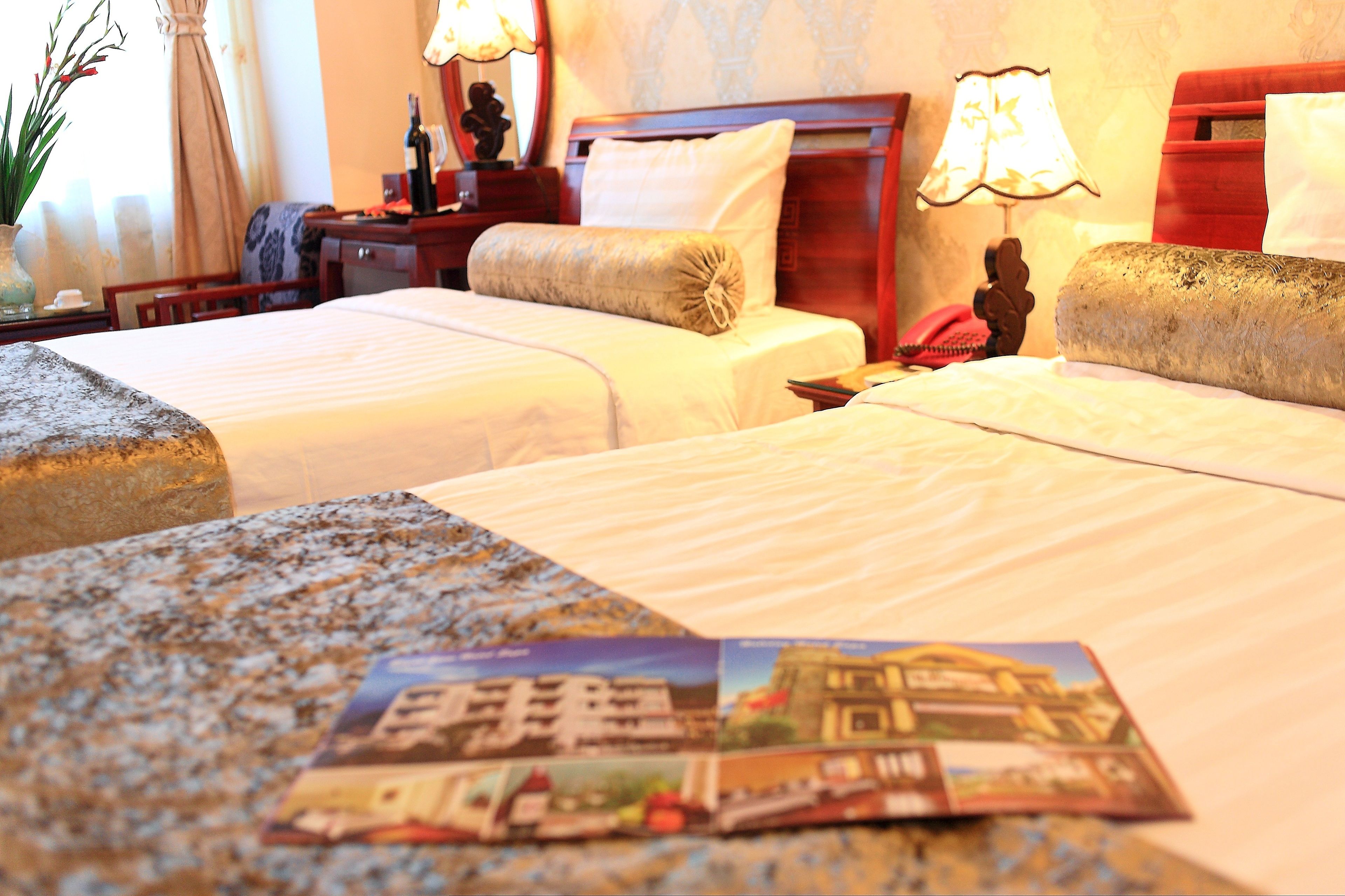 A hotel room with two beds, a nightstand, a lamp, and a magazine on the bed.