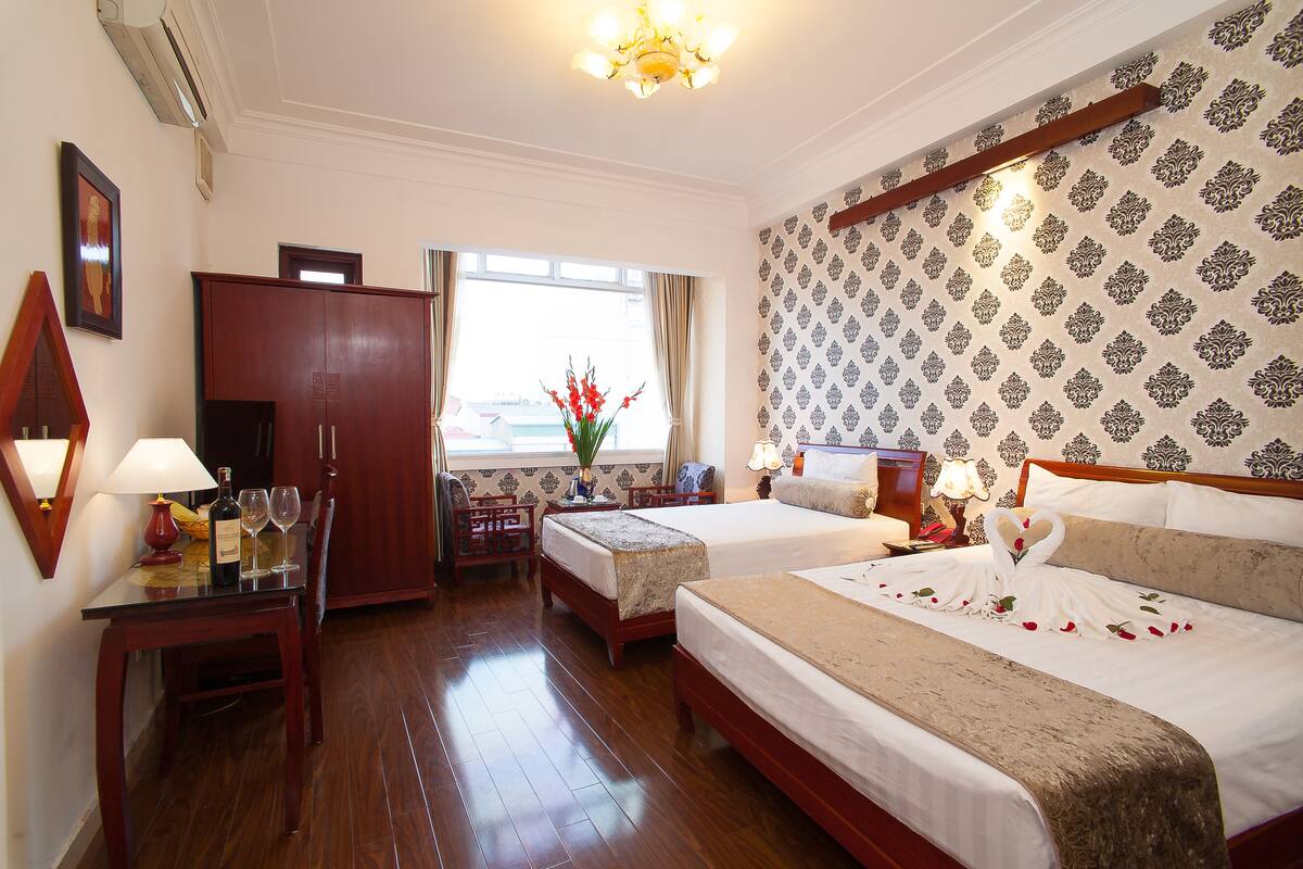 A hotel room with two beds, a desk with a lamp, a chair, a wardrobe, and a window with a view.