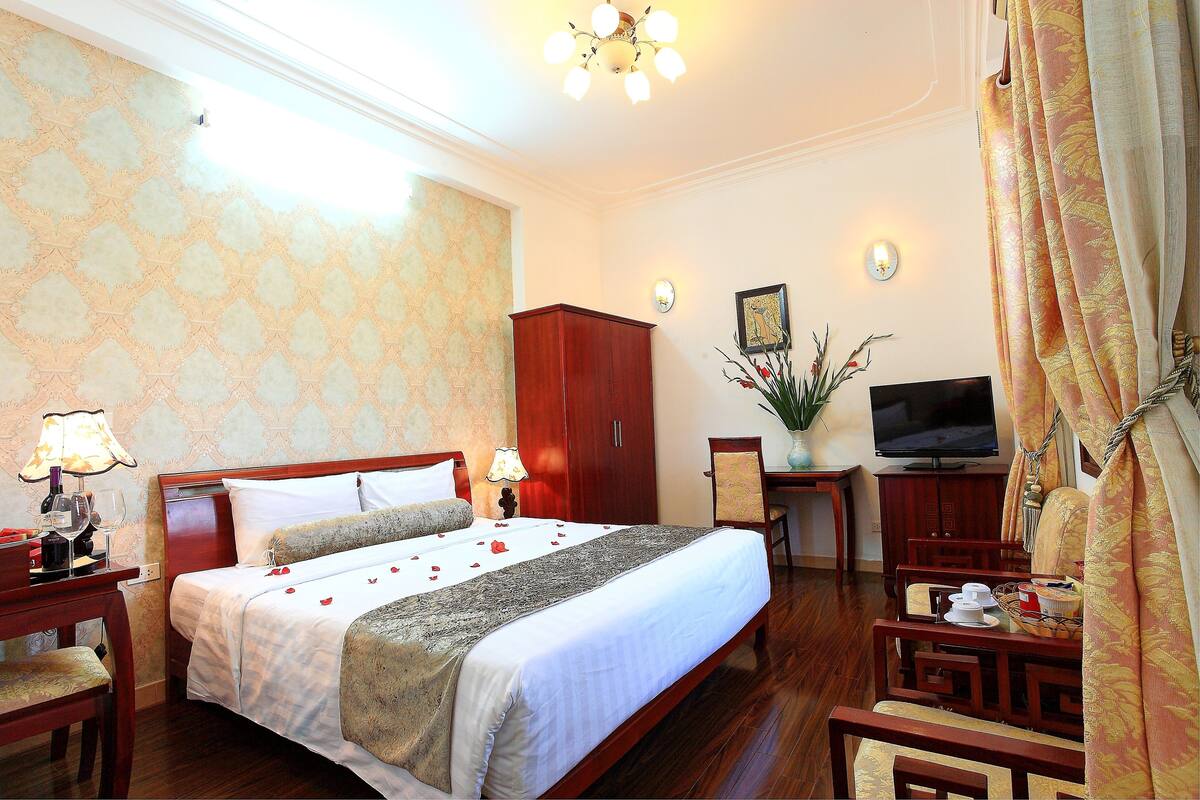 A hotel room with a bed, bedside tables, a TV, and a desk.