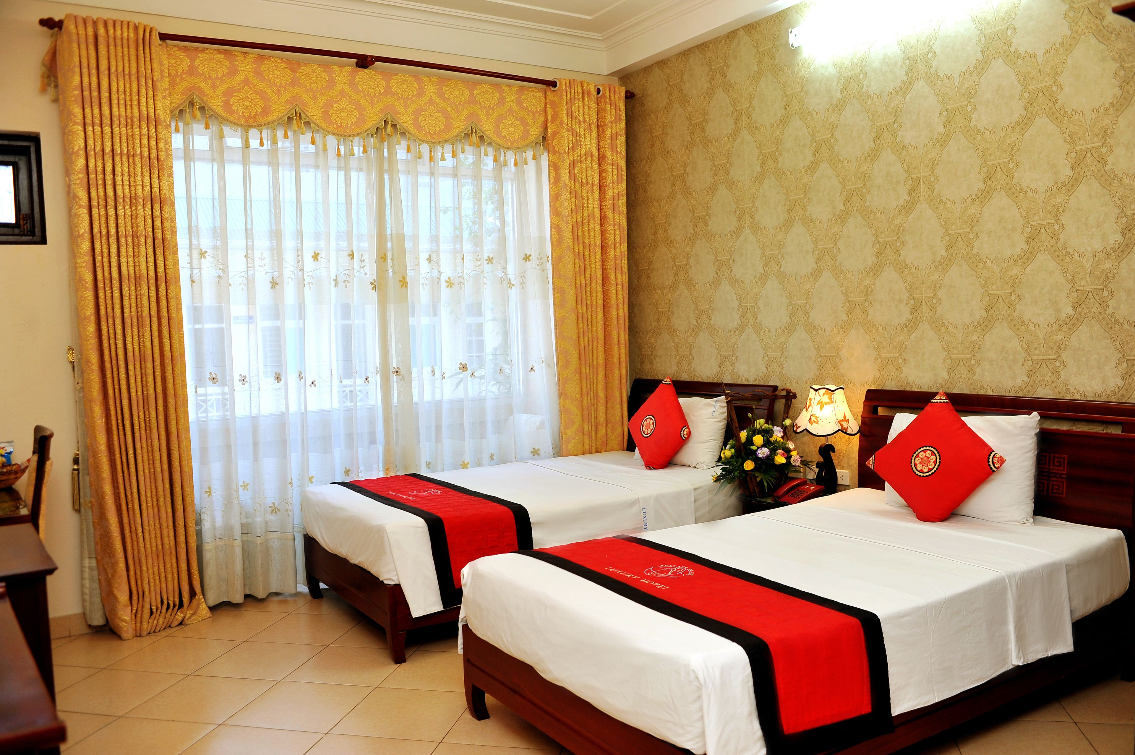 Une chambre d’h ôtel avec deux lits, chacun recouvert d’une couverture rouge et blanche, doté d’une tête de lit en bois et agrémenté d’une table de chevet avec une lampe.