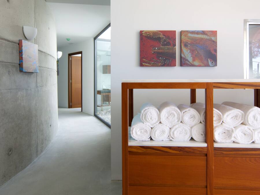 Un pasillo con un banco de madera que sostiene toallas enrolladas, una pared de concreto y dos cuadros abstractos en la pared.