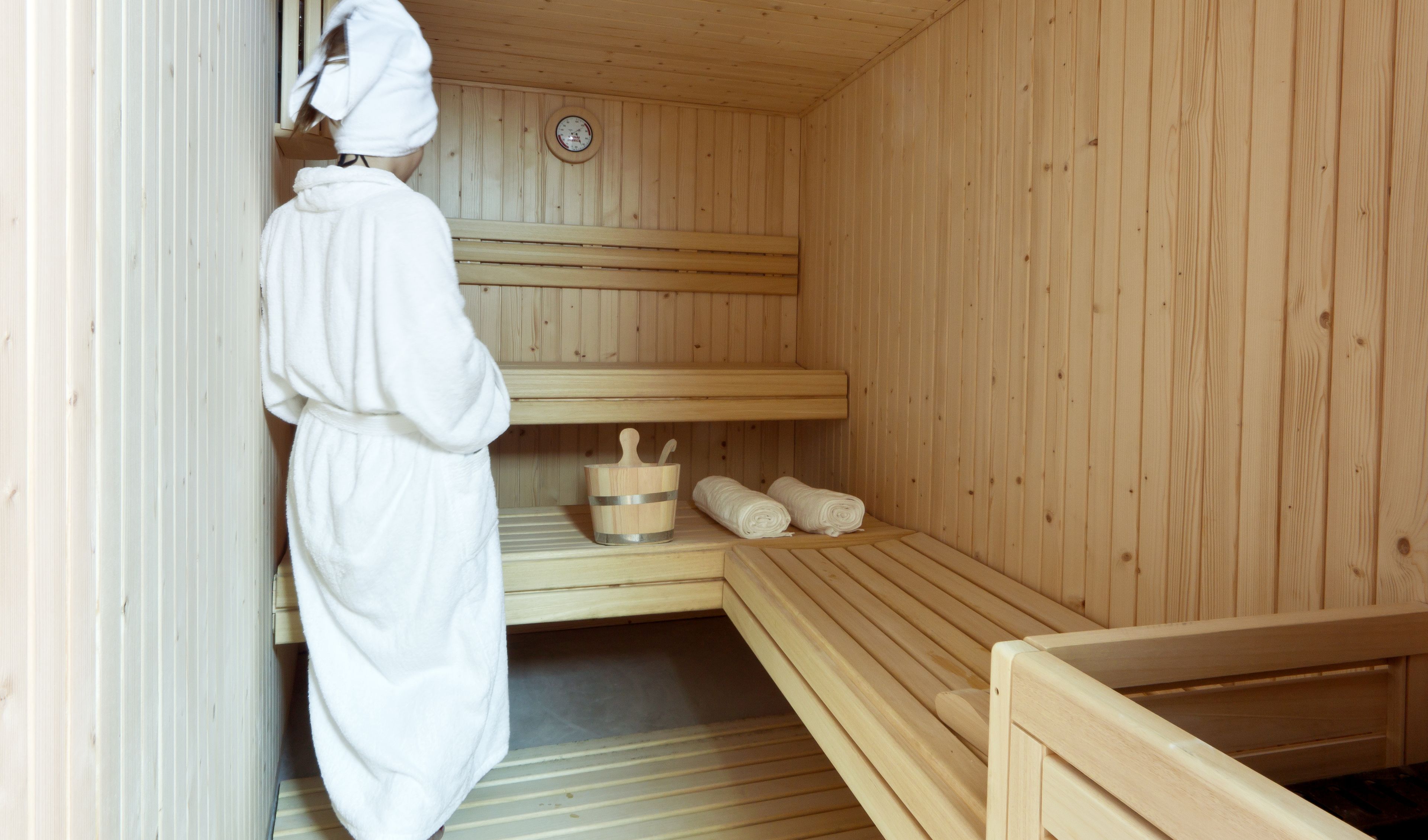 Un cuarto de sauna con bancos de madera, un balde de madera con una cuchara y toallas.