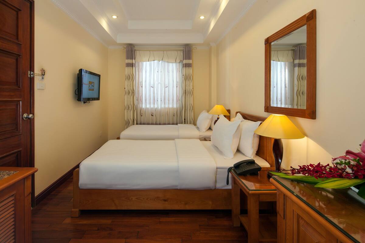 A hotel room with two beds, a desk with a lamp, a telephone, and a mirror on the wall.