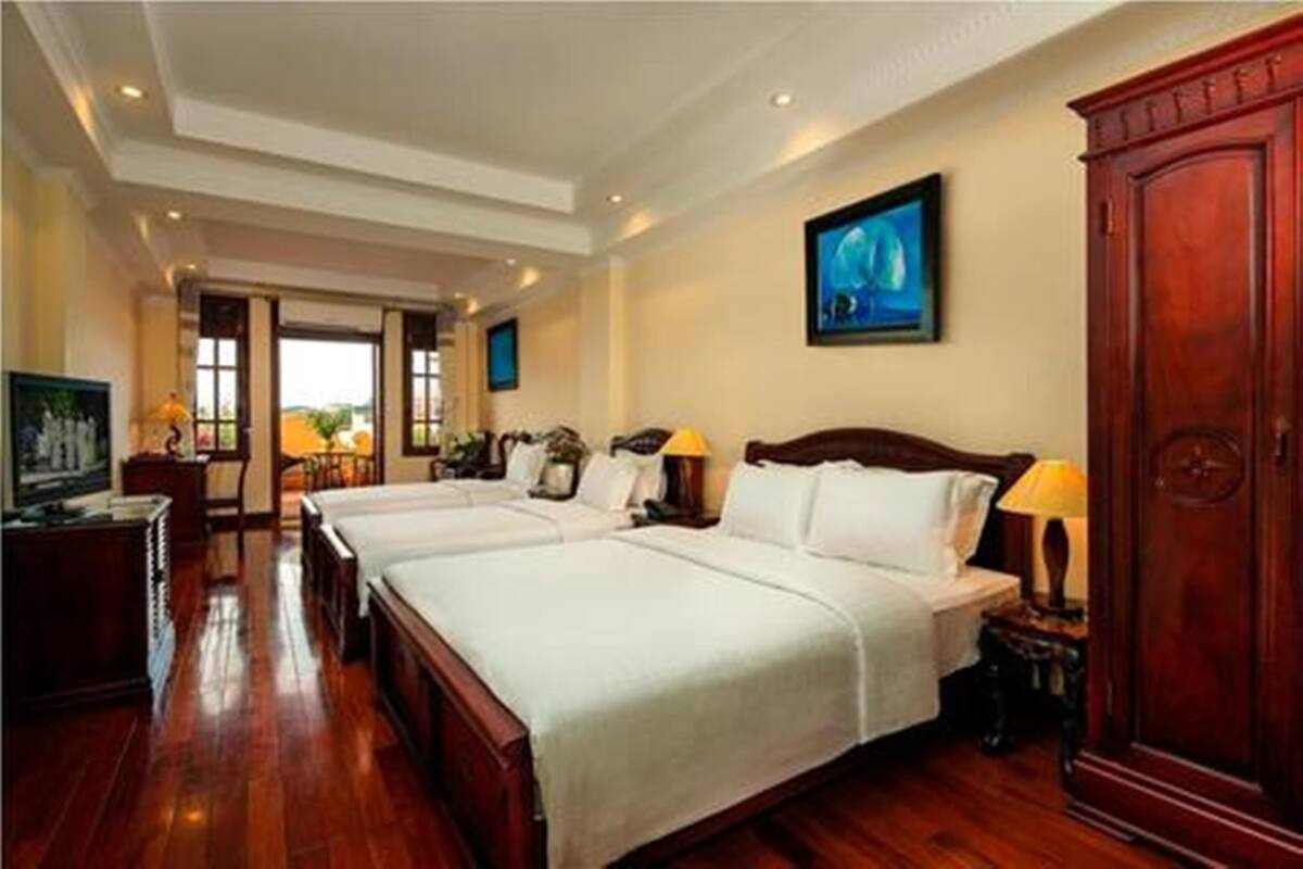 A hotel room with two beds, wooden flooring, a large wardrobe, and a painting on the wall.
