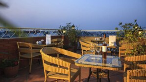 An outdoor patio with wicker furniture, a glass table, and a bottle of wine. - Lucky 3 Hotel & Travel  (Hanoi)