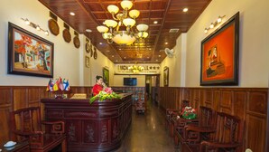 A reception area with a wooden reception desk, chairs, a chandelier, and framed artwork on the walls. - Lucky 3 Hotel & Travel  (Hanoi)