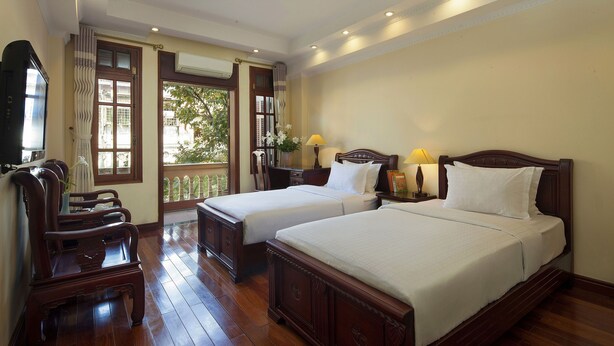 A hotel room with two beds, wooden furniture, a TV, and a balcony with a view. - Lucky 3 Hotel & Travel  (Hanoi)