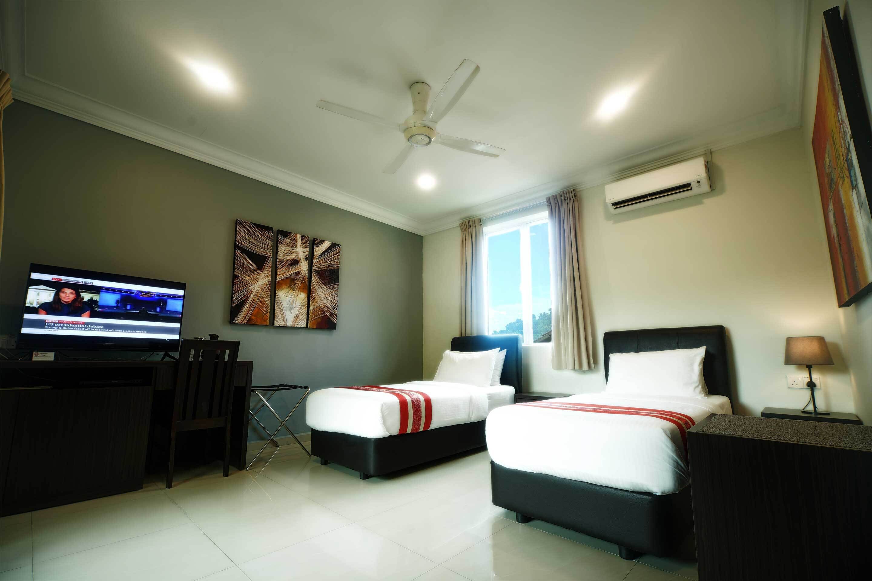 A hotel room with two beds, a desk, a TV, and artwork on the walls.