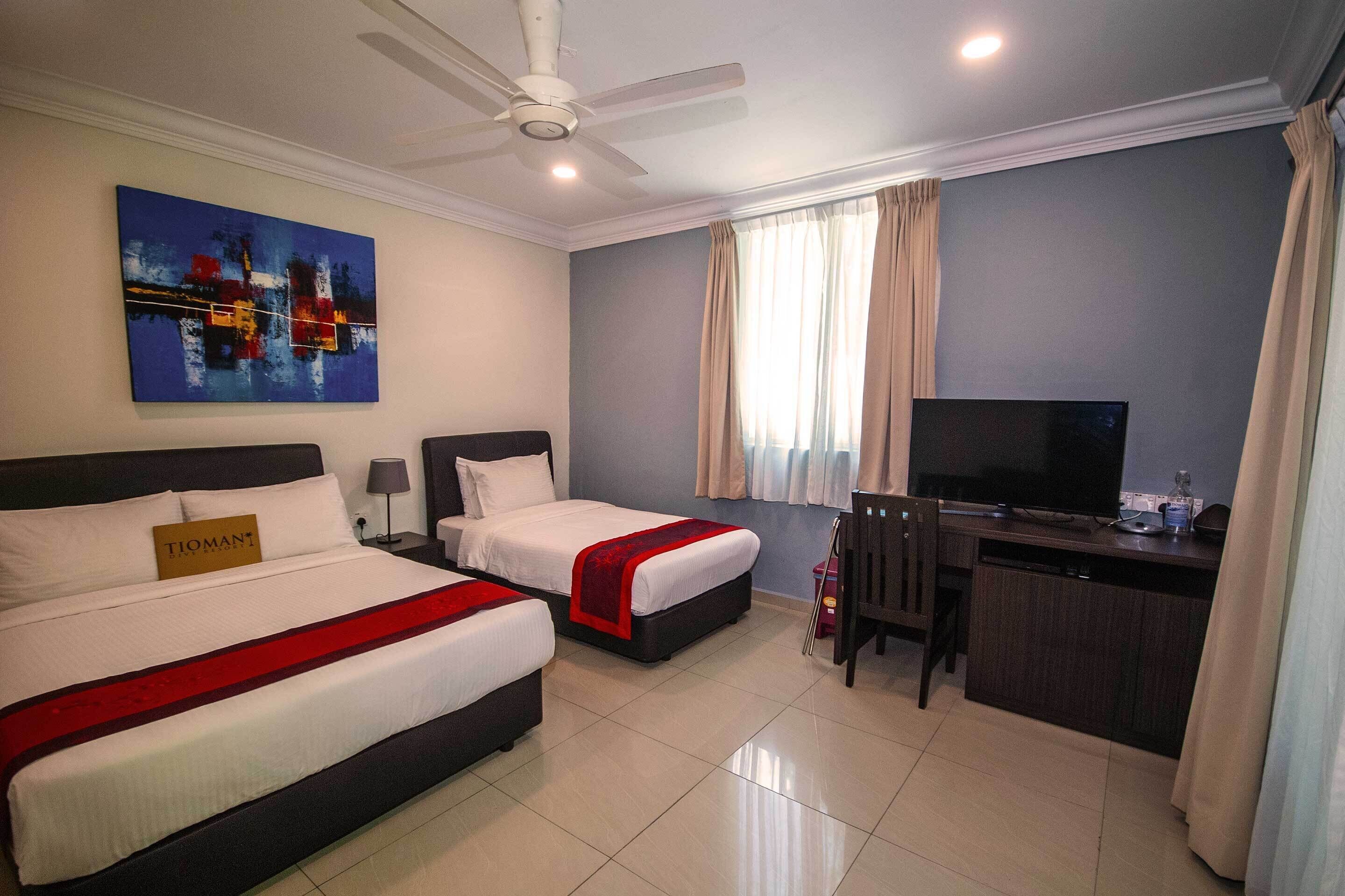 A hotel room with two beds, a desk, a television, and a ceiling fan.