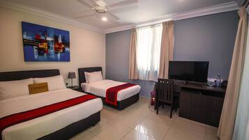 A hotel room with two beds, a desk, a television, and a ceiling fan.