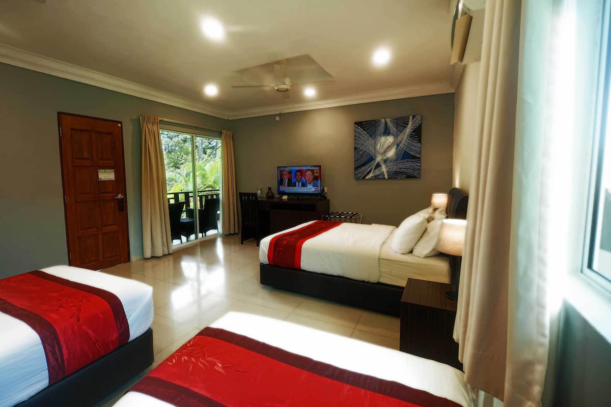 Ein Hotelzimmer mit zwei Betten, einem Fernseher, einem Deckenventilator und einem Balkon mit Vorhängen.