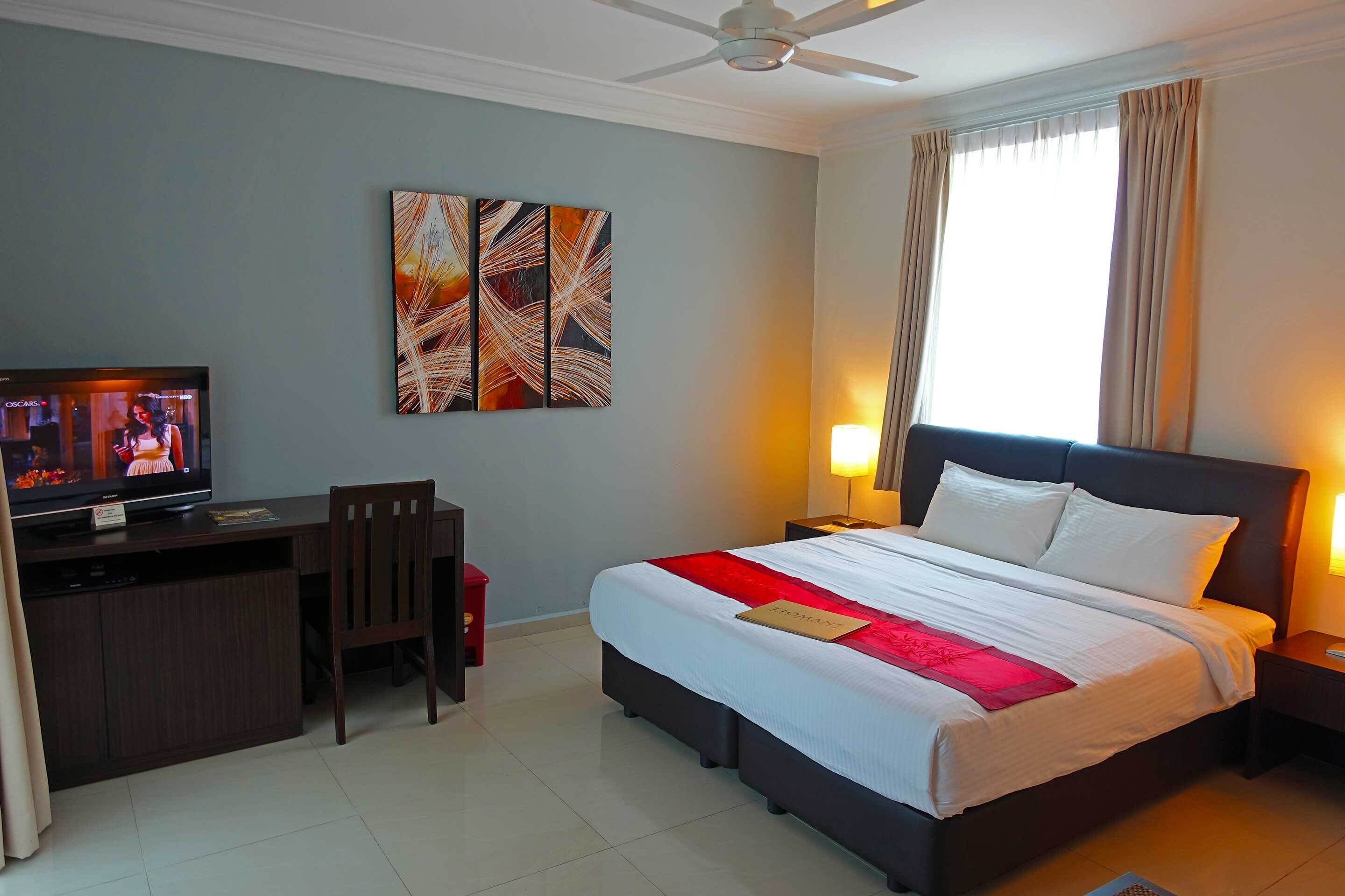 A hotel room with a bed, desk, television, and artwork on the wall.
