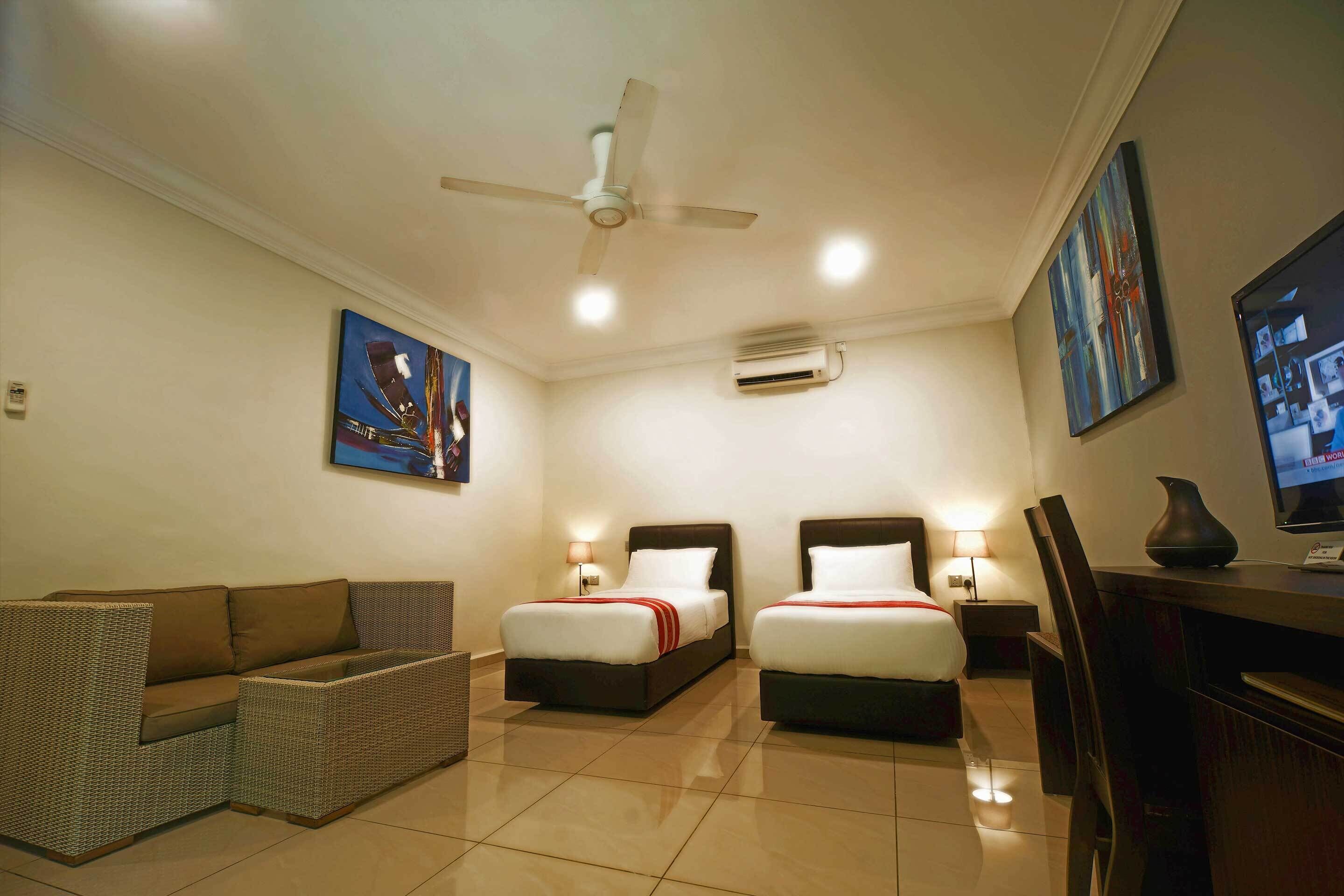 A hotel room with two beds, a sofa, a TV, and a ceiling fan.