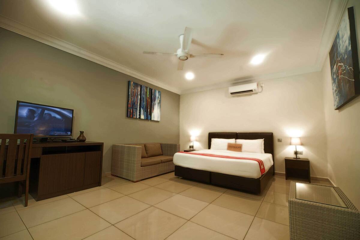 Ein Hotelzimmer mit Bett, Fernseher, Schreibtisch, Stuhl, Sofa und Bildern an der Wand.