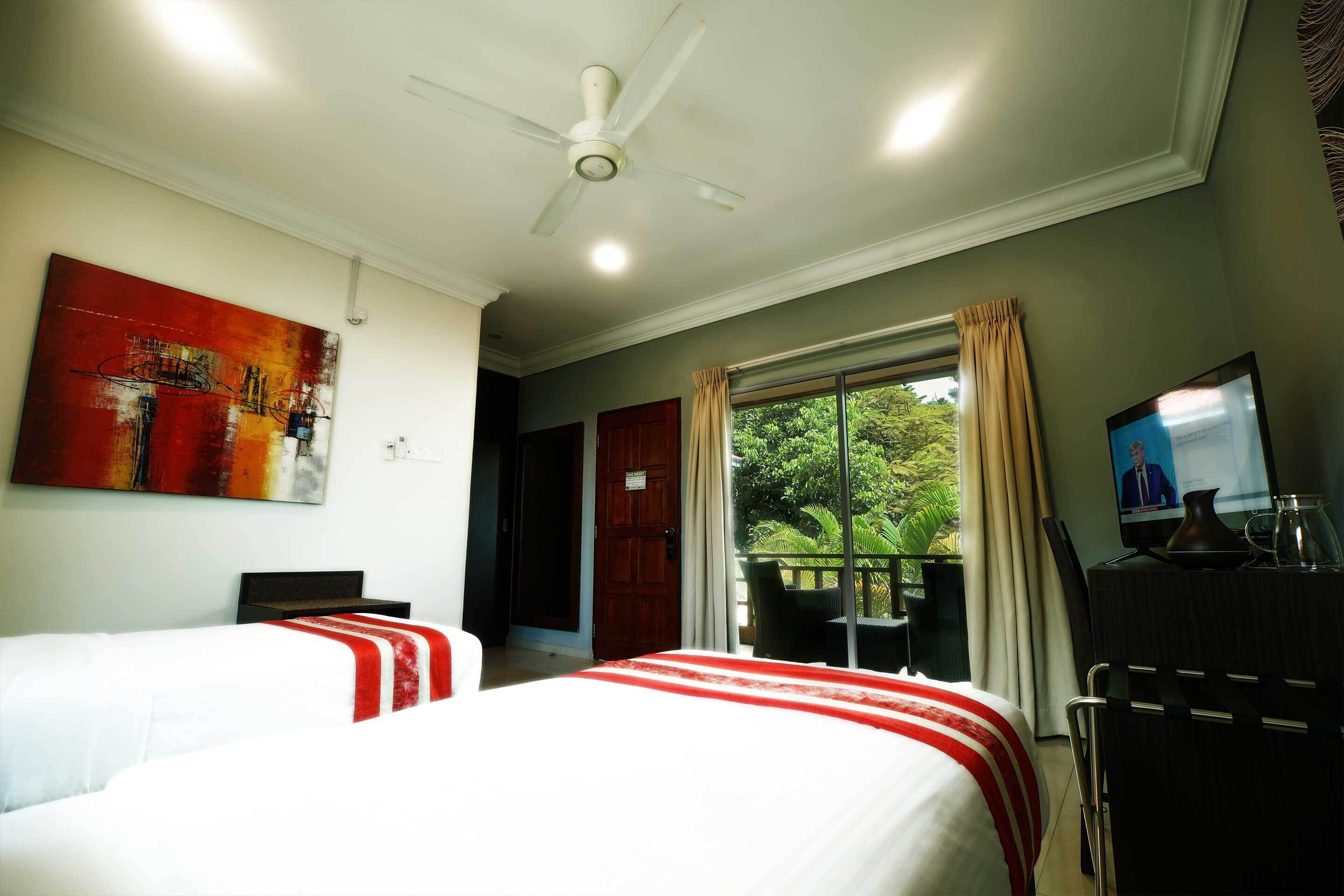 A hotel room with two beds, a ceiling fan, a TV, and a window with curtains.