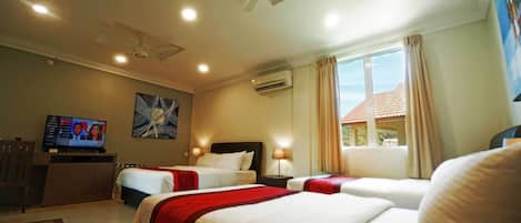 Una habitación de hotel con dos camas, televisión, ventilador de techo y ventana con cortinas.