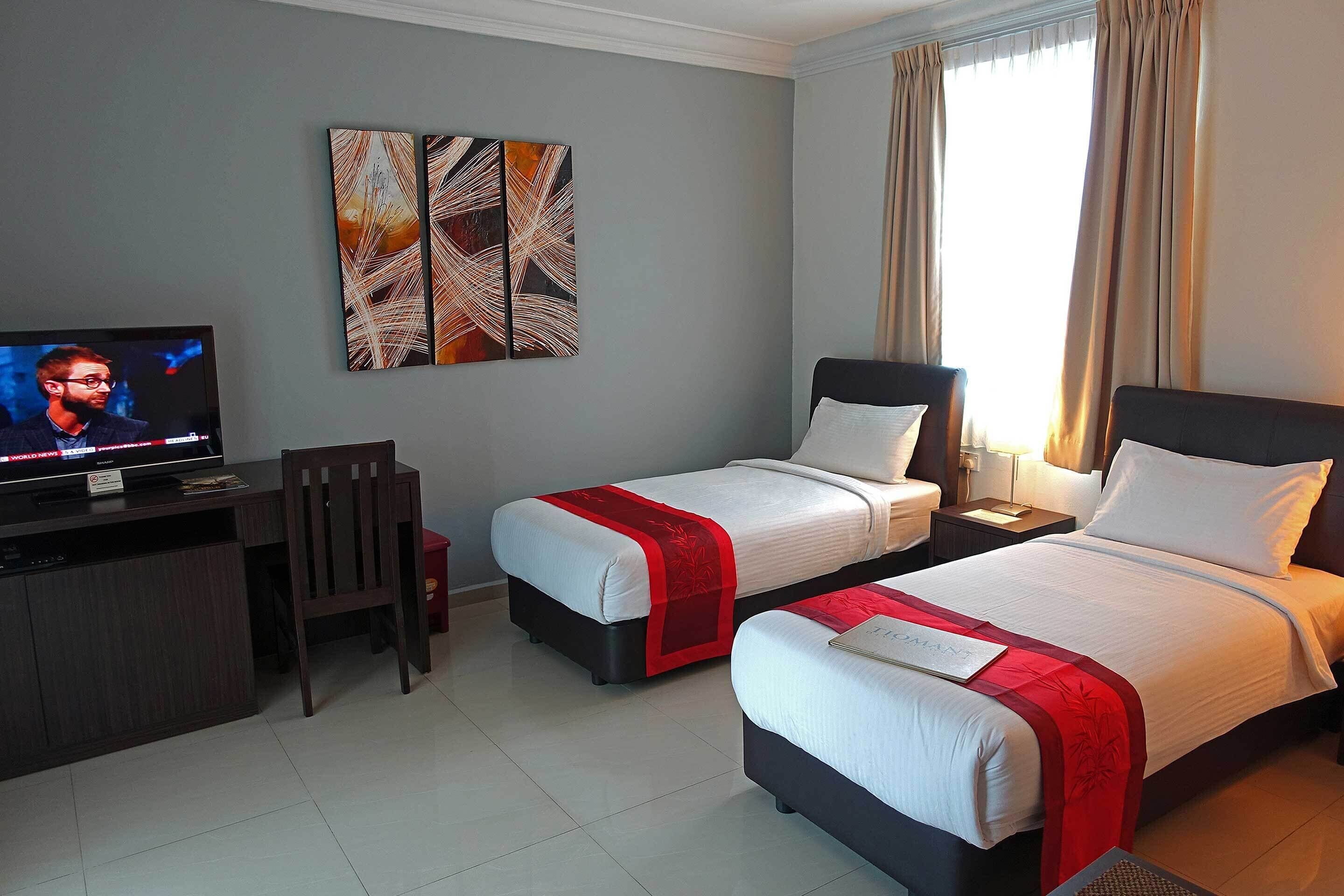 Habitación de hotel con dos camas, un escritorio, un televisor y obras de arte en la pared.