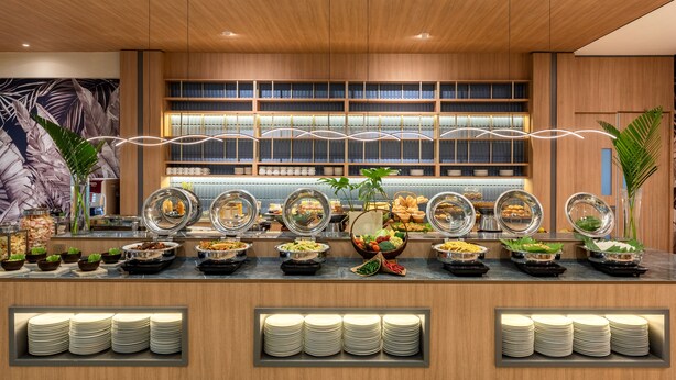 A buffet area with various food stations, including fruits, vegetables, and prepared dishes, with neatly stacked plates at the front. - Oakwood Hotel & Apartments Taman Mini Jakarta (Jakarta)