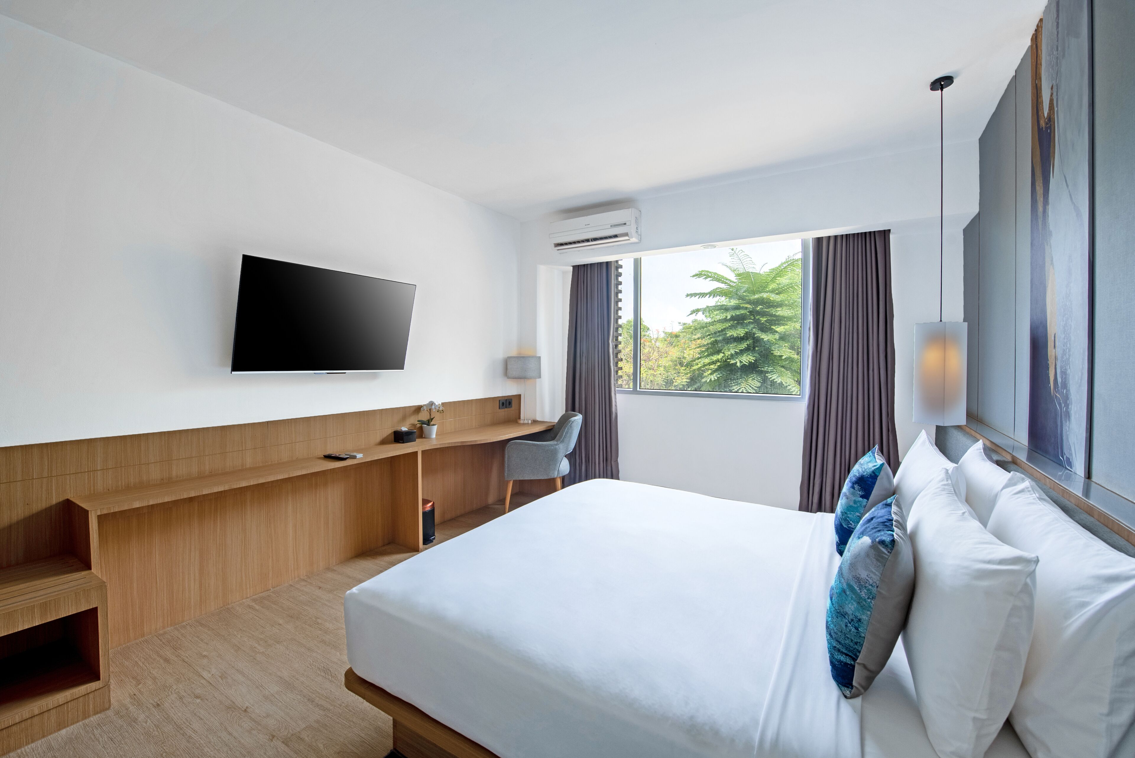 Ett modernt hotellrum med en stor säng, ett skrivbord, en platt-TV och ett fönster med gardiner.