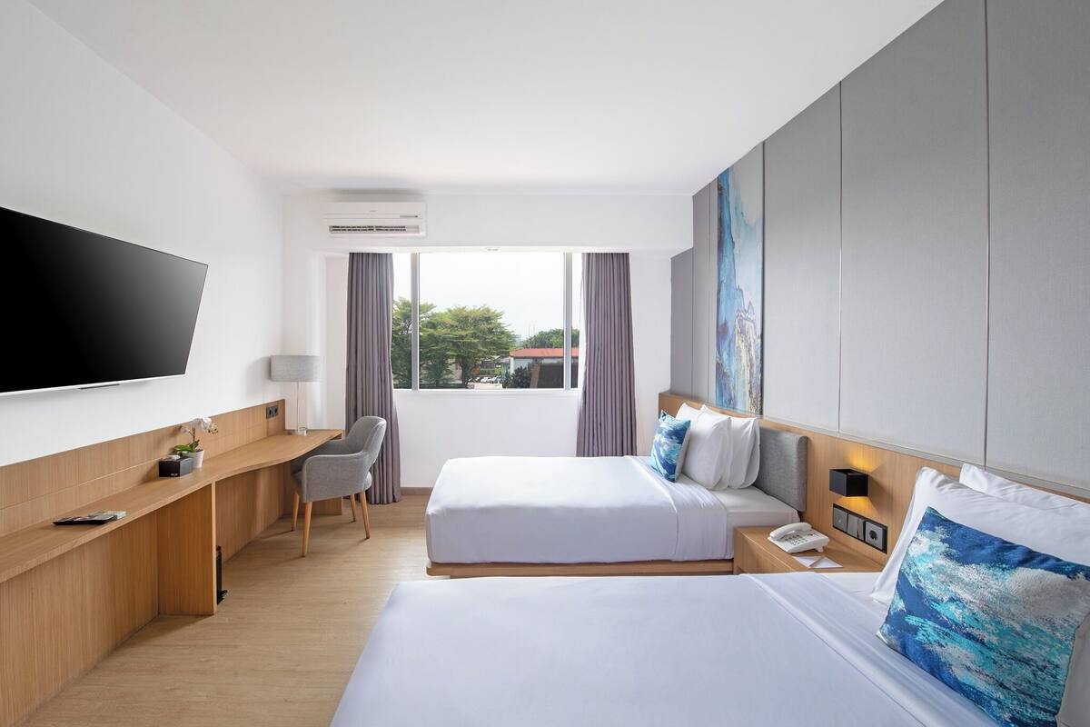 Ein Hotelzimmer mit einem Bett, einem Schreibtisch, einem Sessel, einem Fernseher und einem Fenster.