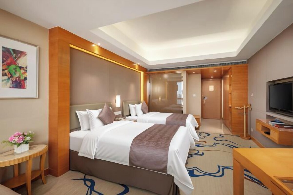 A hotel room with two beds, a TV, a desk, and a mirror.