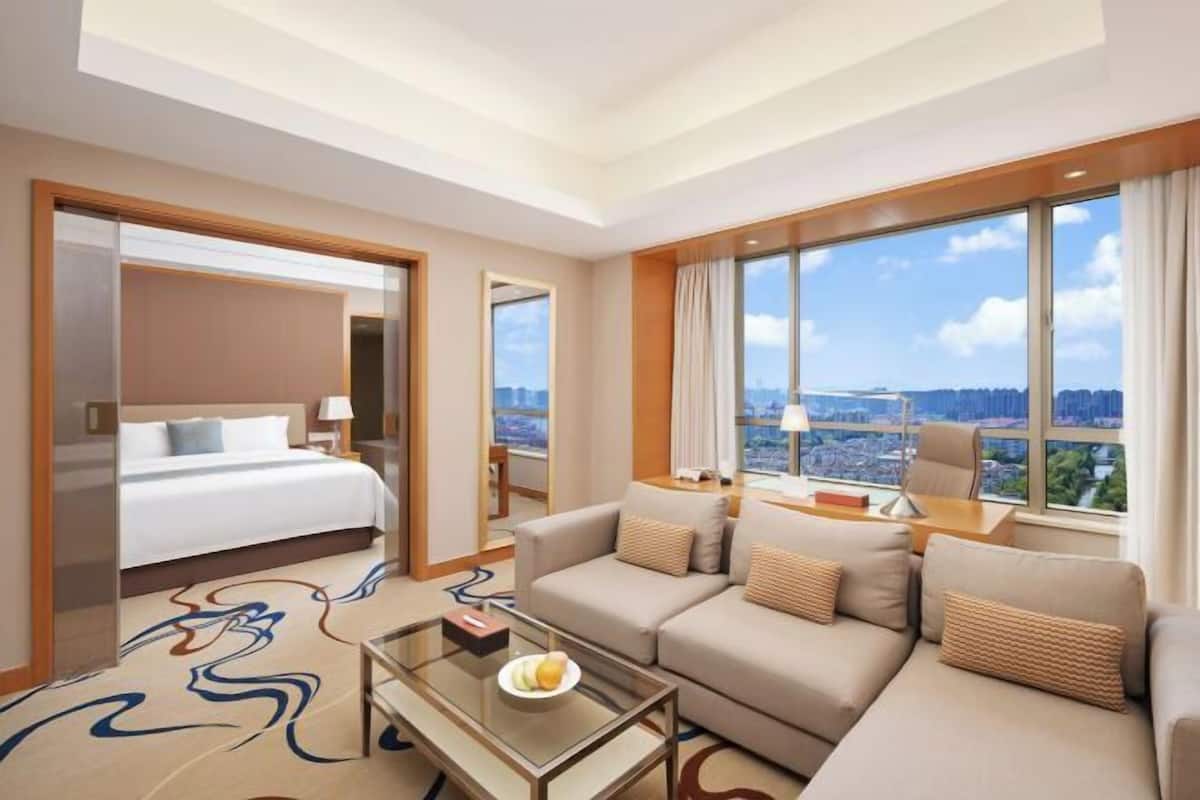 Une chambre d’hôtel équipée d’un lit, d’un canapé, d’une table basse et de grandes fenêtres donnant sur la ville.