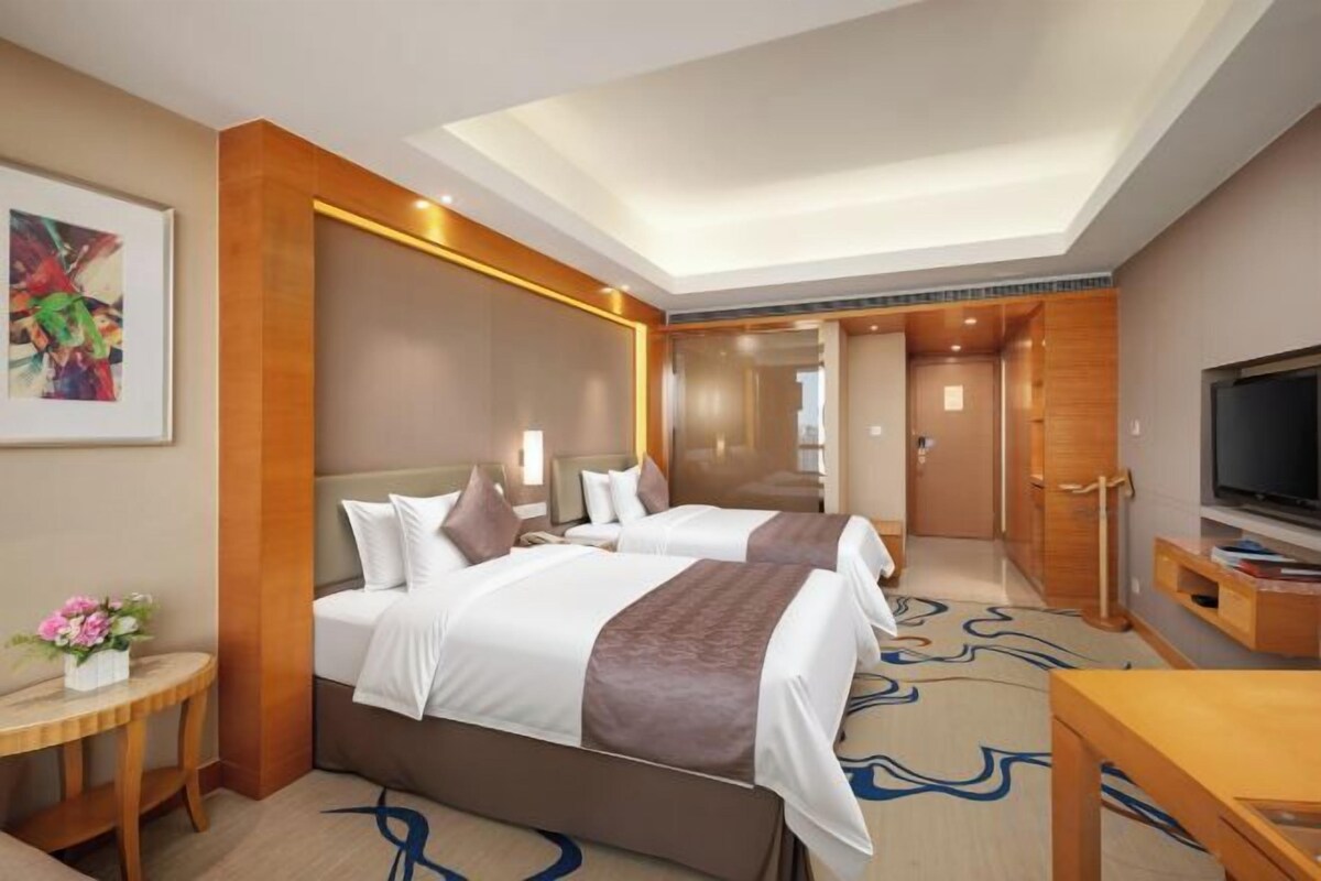 Ein Hotelzimmer mit zwei Betten, einem Fernseher, einem Schreibtisch und einem Spiegel.