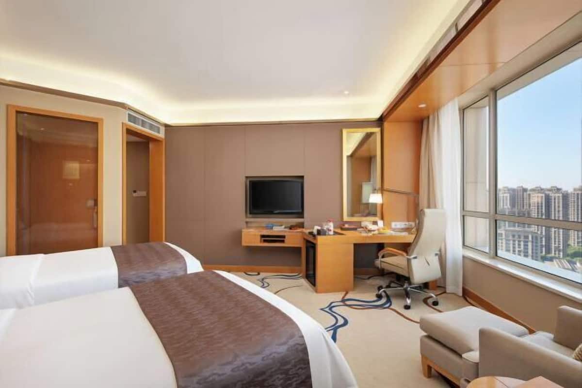 Une chambre d’hôtel avec deux lits, un bureau, une chaise, une télévision et une grande fenêtre donnant sur la ville.
