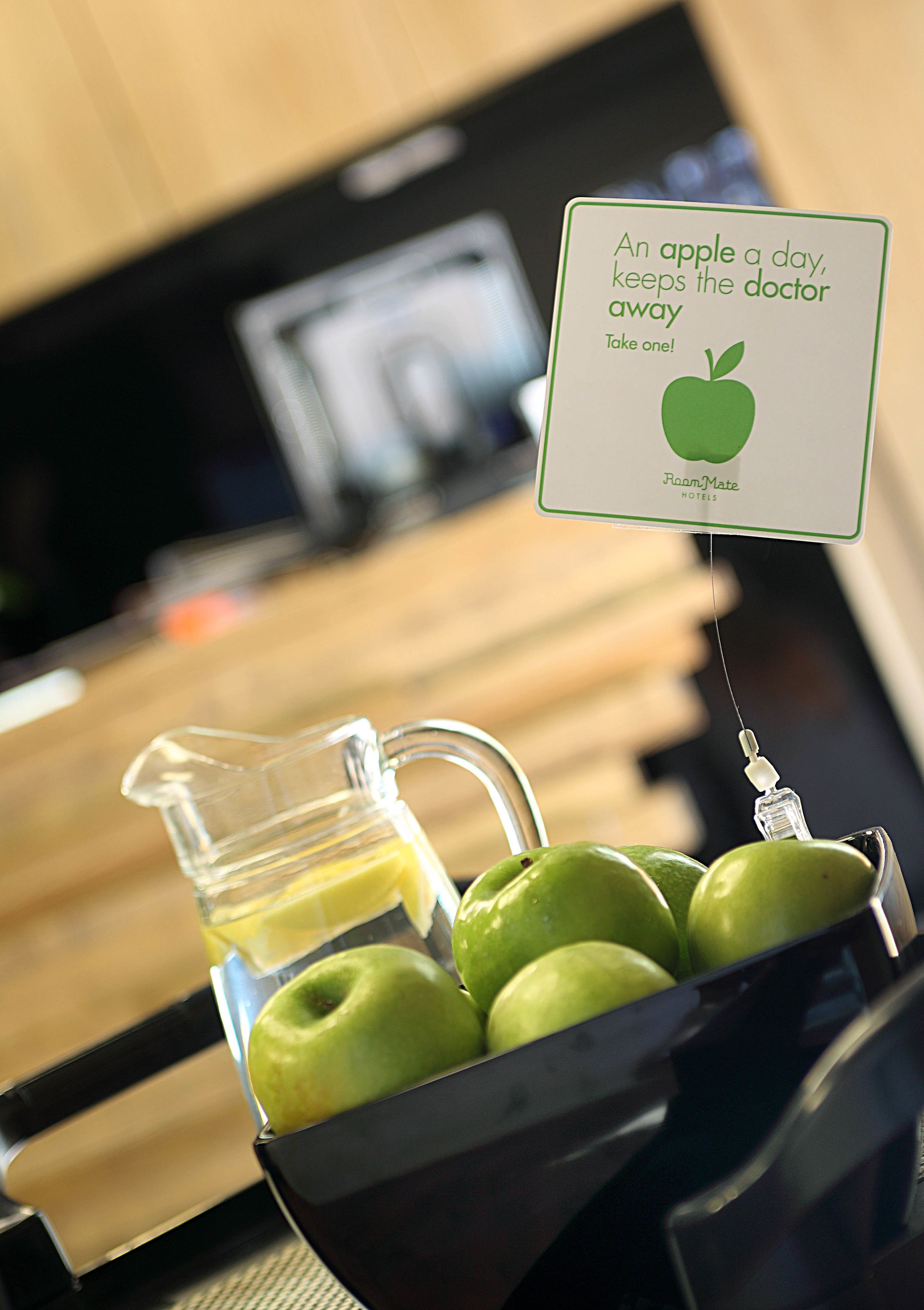 A kitchen area with a sign promoting the health benefits of apples, a pitcher of apple juice, and a bowl of green apples.