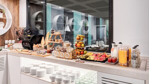 Um buffet de café da manhã com diversas opções de alimentos e bebidas, incluindo frutas, doces e uma máquina de café.