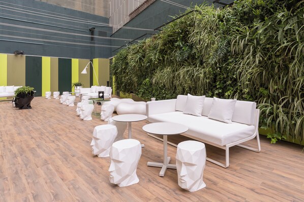 Un área de descanso moderna con un sofá blanco, mesas redondas y taburetes geométricos.