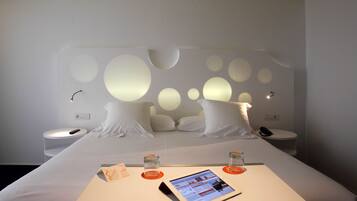 A modern hotel room with a large bed, bedside tables, a bedside lamp, and a tablet displaying a menu.
