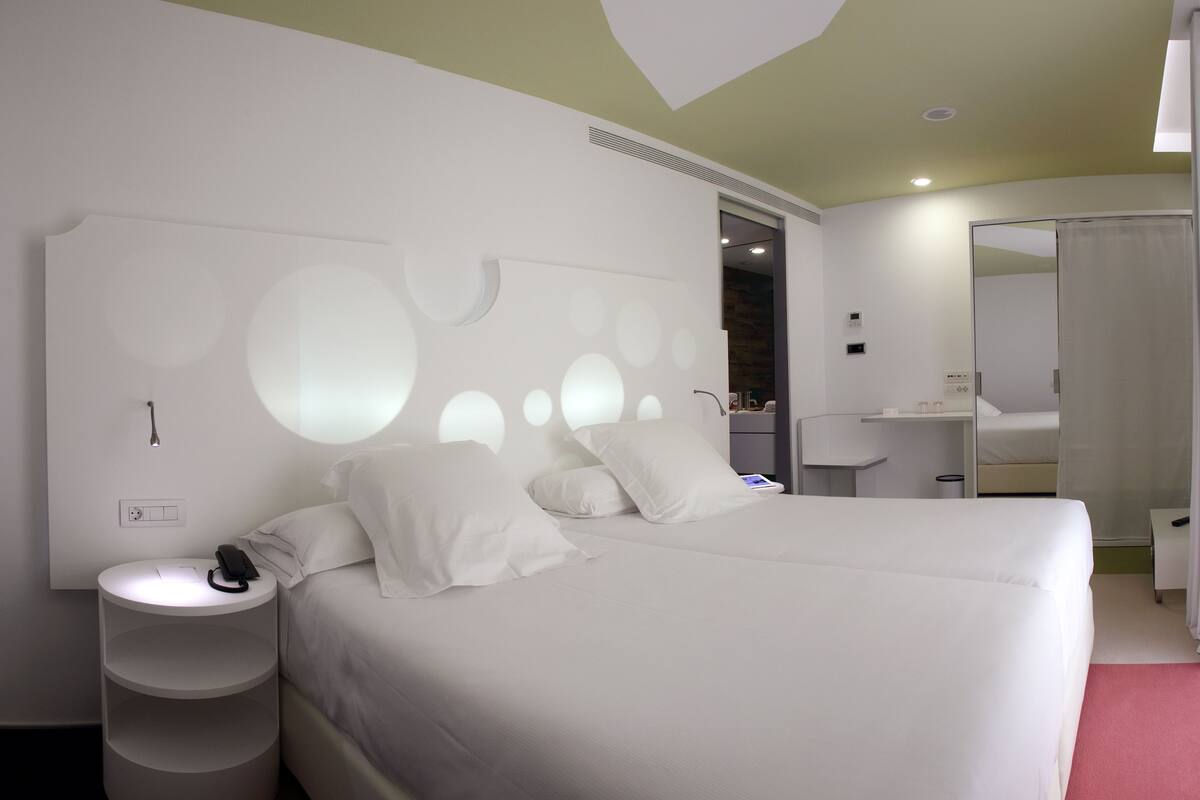 Habitación de hotel moderna con una cama grande, una mesita de noche con un teléfono, un espejo y un estante pequeño.
